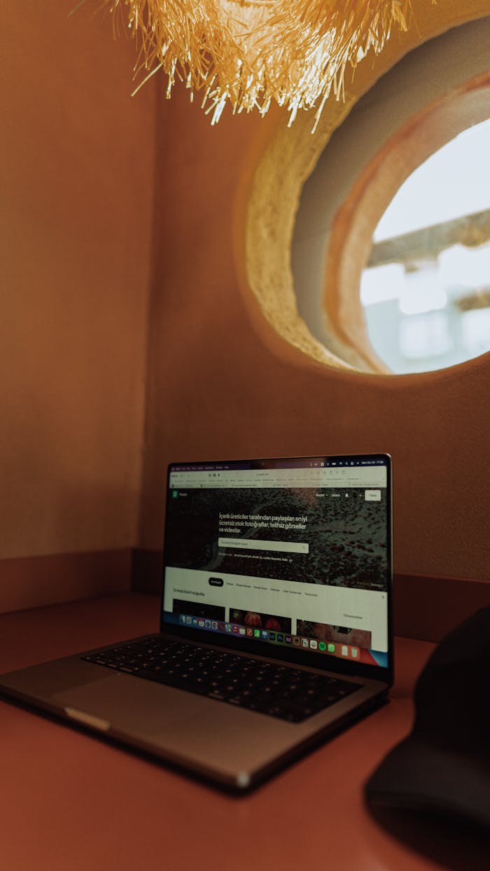 A laptop displaying a website in a warm, cozy interior setting near a circular window.