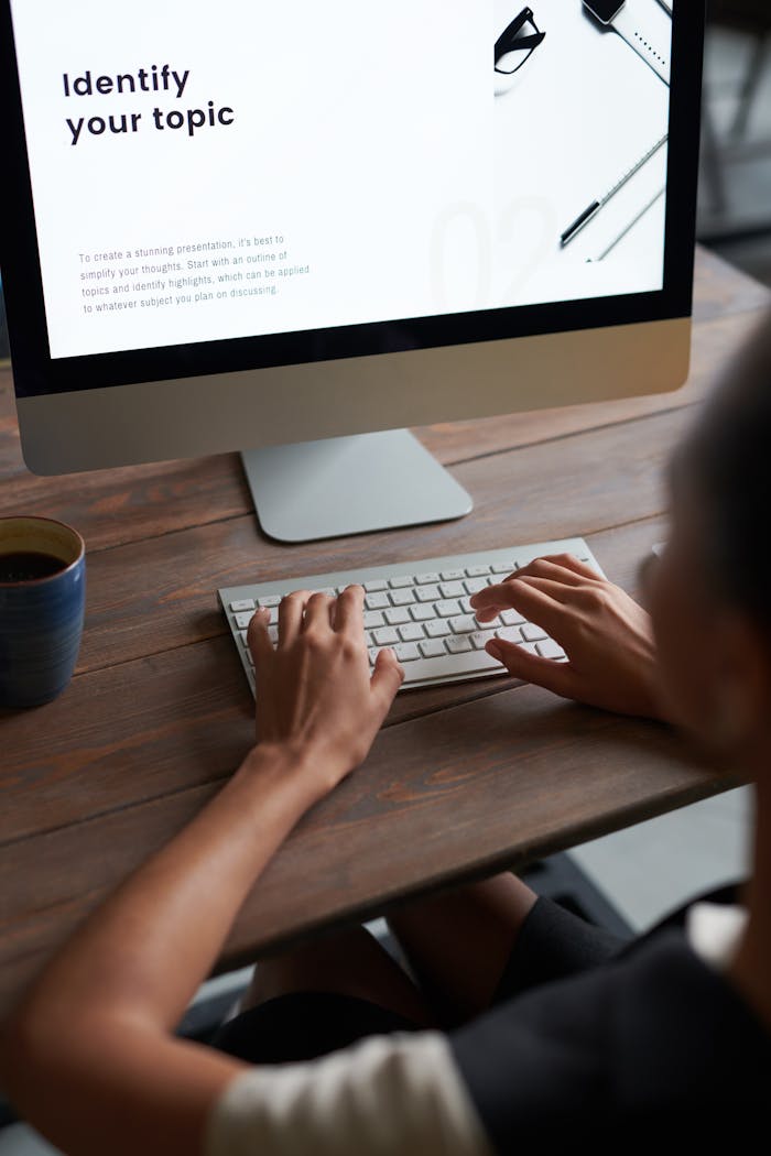 Person working on a digital project at a wooden desk with a computer and coffee.
